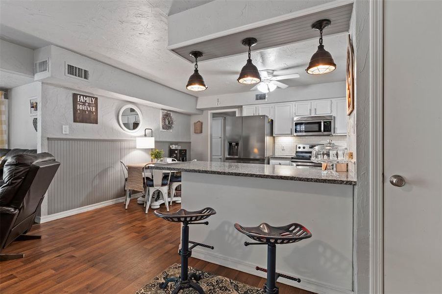 Kitchen featuring white cabinets, backsplash, dark wood-type flooring, stainless steel appliances, and a kitchen bar