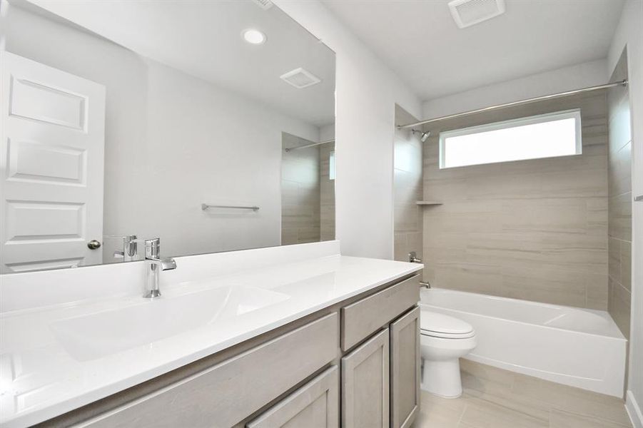 Secondary bath features tile flooring, bath/shower combo with tile surround, light stained wood cabinets, beautiful light countertop. Sample photo of completed home with similar floor plan. Actual colors and selections may vary.