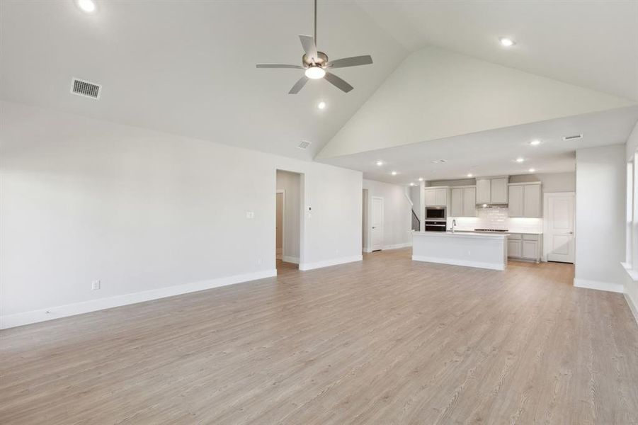 Unfurnished living room with light hardwood / wood-style flooring, high vaulted ceiling, and ceiling fan