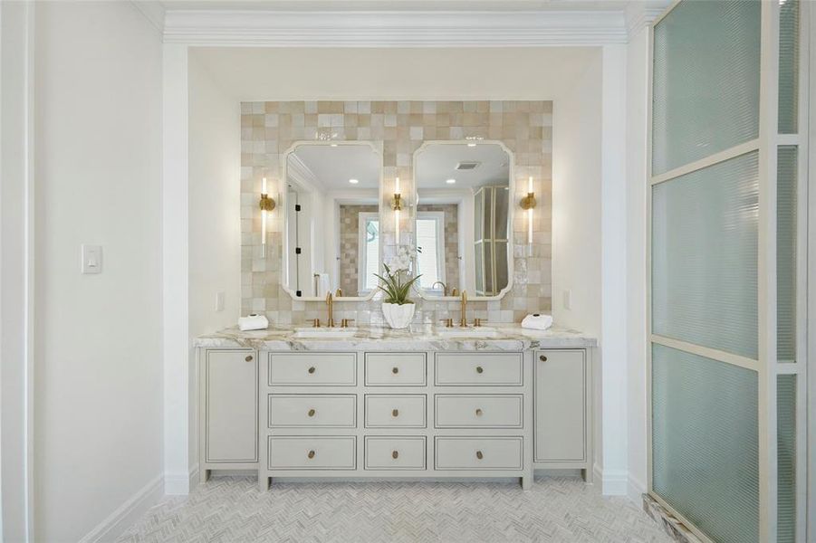 Primary suite's one-of-a kind vanity with double mirrors, elegant countertop, and a well-considered design featuring gold fixtures and tasteful wall tiles.