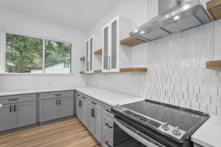 Kitchen featuring electric stove, backsplash, island range hood, light stone counters, and light hardwood / wood-style floors