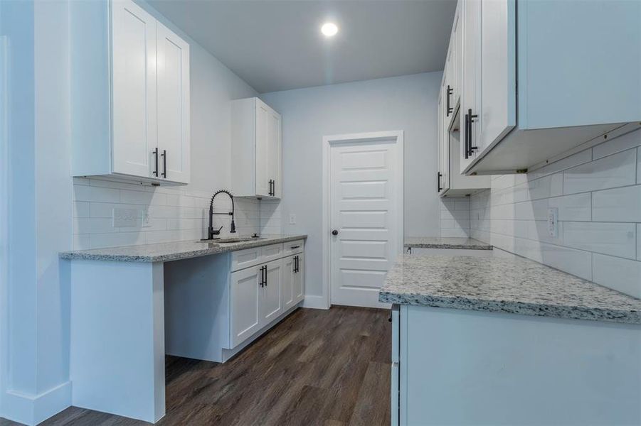 Kitchen with light stone counters, backsplash, sink, white cabinets, and dark wood-type flooring