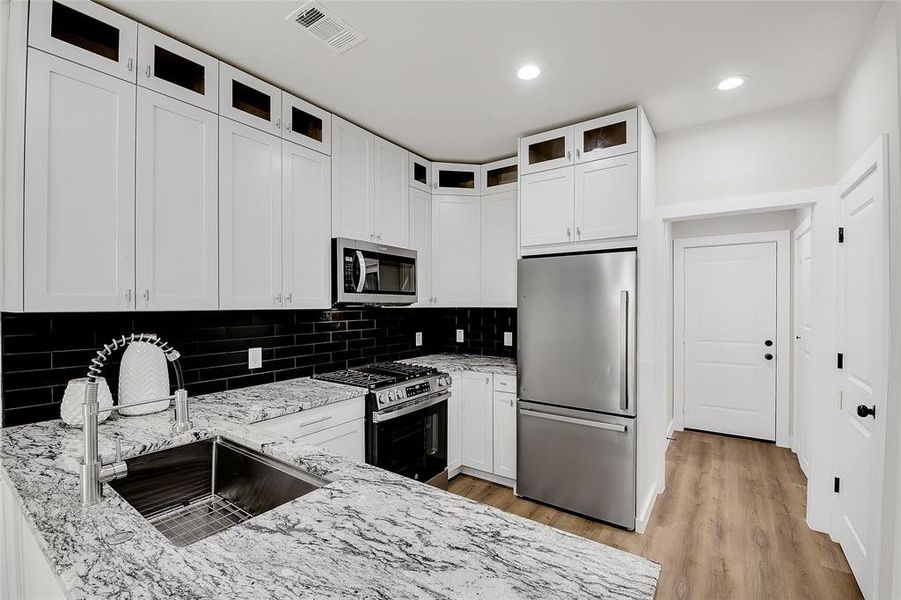 Kitchen featuring light wood-type flooring, light granite counters, sink, white cabinetry, and appliances with stainless steel finishes