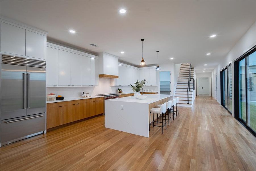 Kitchen featuring built in refrigerator, decorative light fixtures, light hardwood / wood-style flooring, and white cabinetry