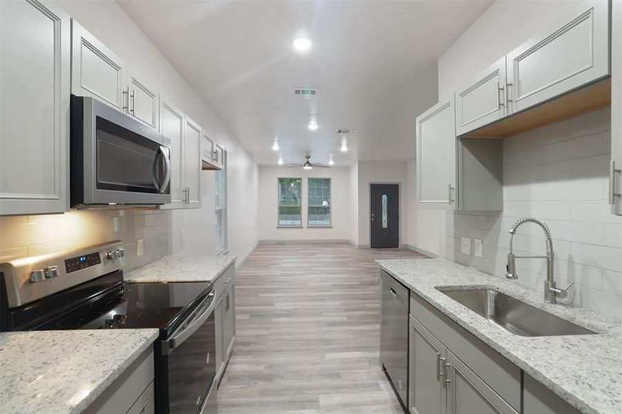 Kitchen with stainless steel appliances, light hardwood / wood-style flooring, backsplash, and sink