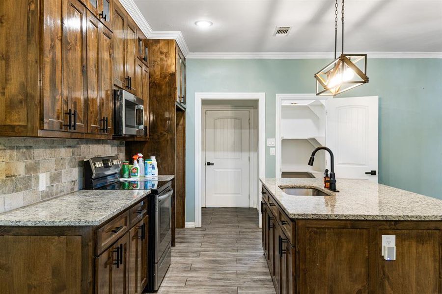 Kitchen with light stone counters, stainless steel appliances, light wood-type flooring, decorative light fixtures, and sink