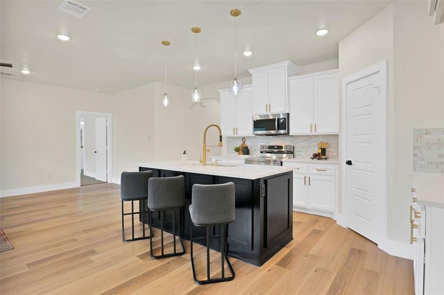 Kitchen with a kitchen island with sink, decorative light fixtures, stainless steel appliances, white cabinets, and light hardwood / wood-style floors