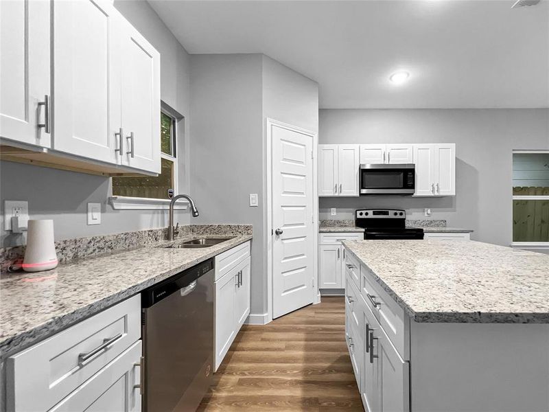 Kitchen with white cabinetry, light stone countertops, stainless steel appliances, hardwood / wood-style floors, and sink