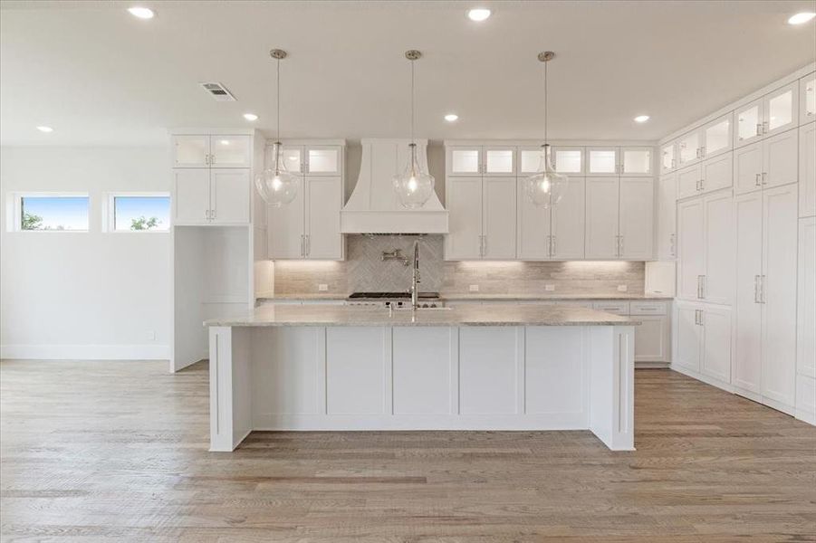 Kitchen with white cabinets, light wood-type flooring, custom range hood, and a kitchen island with sink