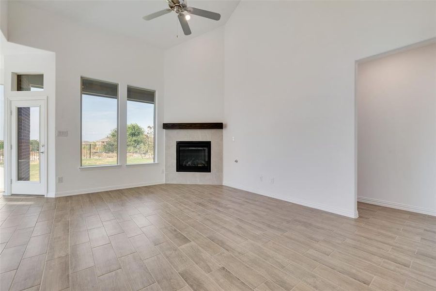 Unfurnished living room with high vaulted ceiling, a tiled fireplace, light wood-type flooring, and ceiling fan