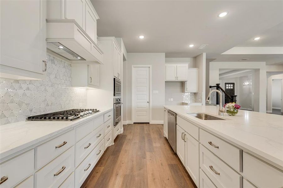 Kitchen featuring appliances with stainless steel finishes, light hardwood / wood-style floors, light stone counters, white cabinets, and sink