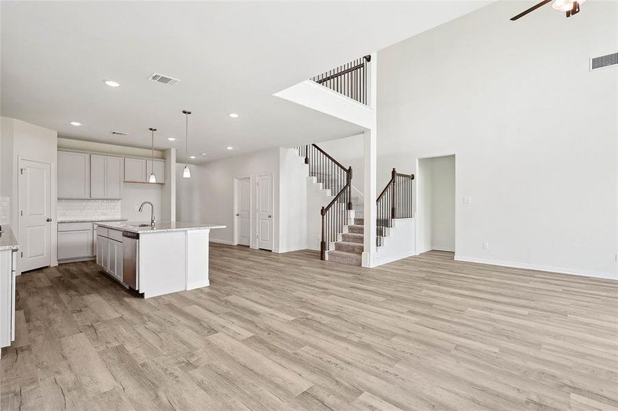 Kitchen featuring light wood-type flooring, backsplash, hanging light fixtures, a towering ceiling, and a kitchen island with sink