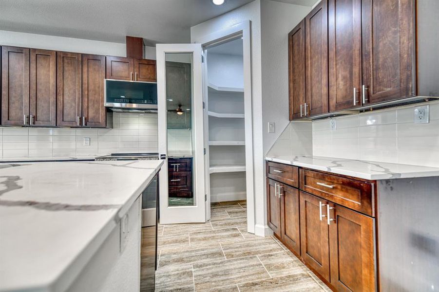 Kitchen with dark brown cabinetry, light hardwood / wood-style flooring, light stone countertops, and backsplash