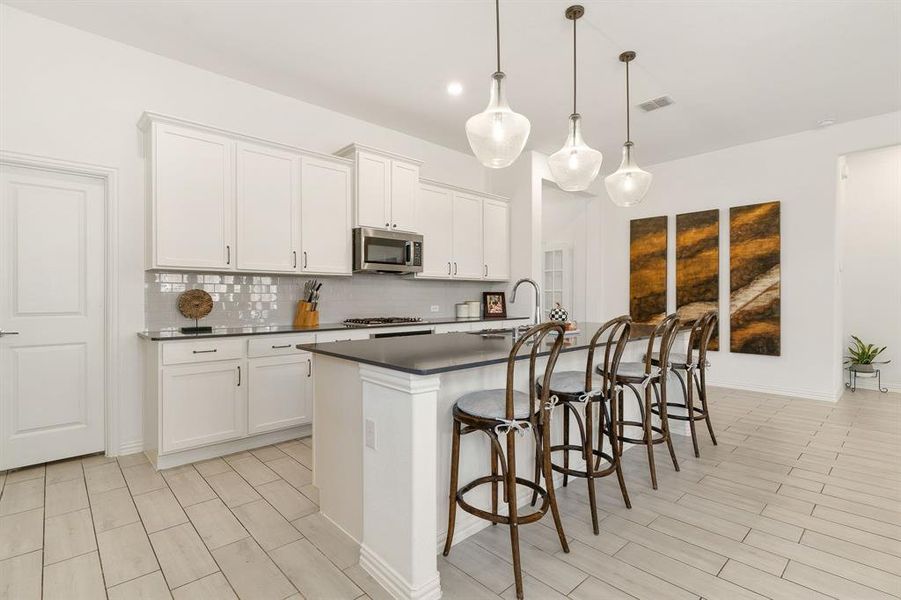 Kitchen featuring tasteful backsplash, a kitchen breakfast bar, white cabinetry, a kitchen island with sink, and pendant lighting