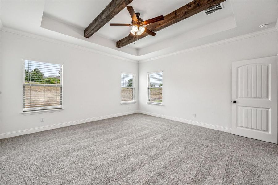 Carpeted spare room with ceiling fan, a raised ceiling, a wealth of natural light, and beam ceiling
