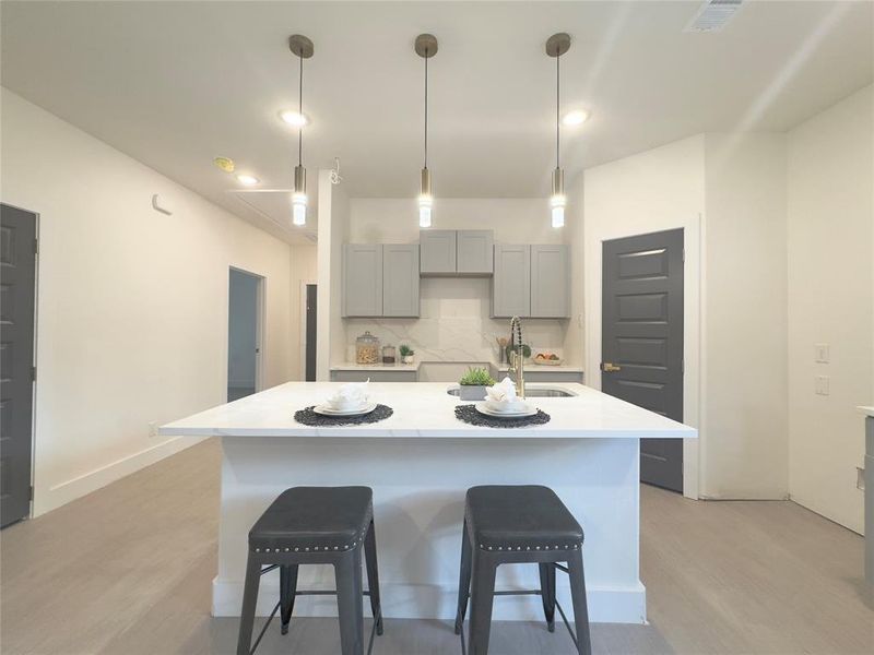 Kitchen with light hardwood / wood-style floors, a kitchen island with sink, pendant lighting, a kitchen bar, and tasteful backsplash