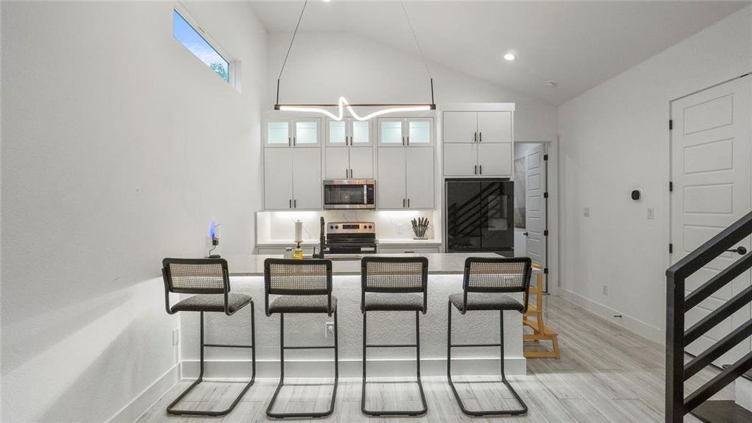 Kitchen with white cabinets, stainless steel appliances, light hardwood / wood-style floors, a kitchen breakfast bar, and high vaulted ceiling