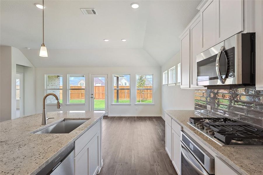 Kitchen featuring vaulted ceiling, stainless steel appliances, white cabinetry, wood-type flooring, and sink