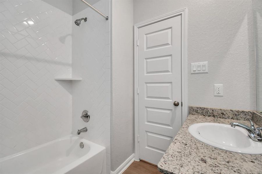 This secondary bathroom features a clean, modern design with a tiled shower and tub combo, a granite countertop, and a sleek under-mount sink. The bright white finishes create a fresh, airy feel, complemented by durable hardware and a five-panel door for added style.