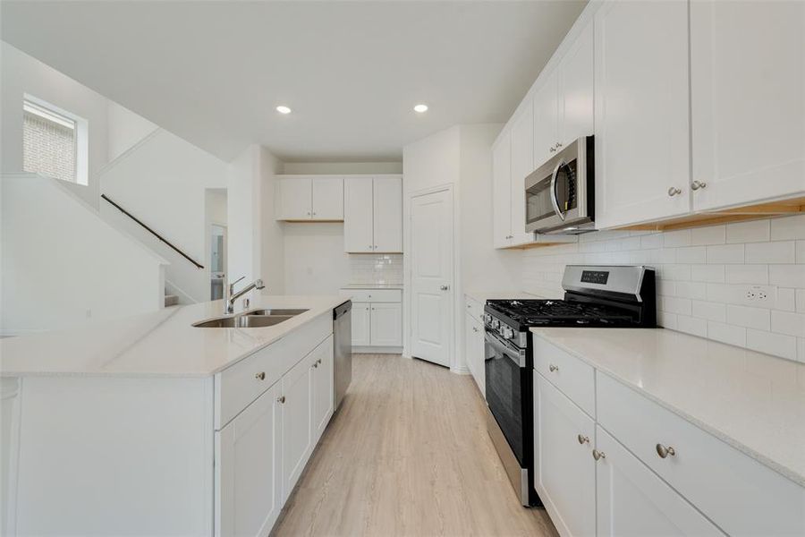 Kitchen featuring stainless steel appliances, a kitchen island with sink, sink, light hardwood / wood-style flooring, and white cabinets