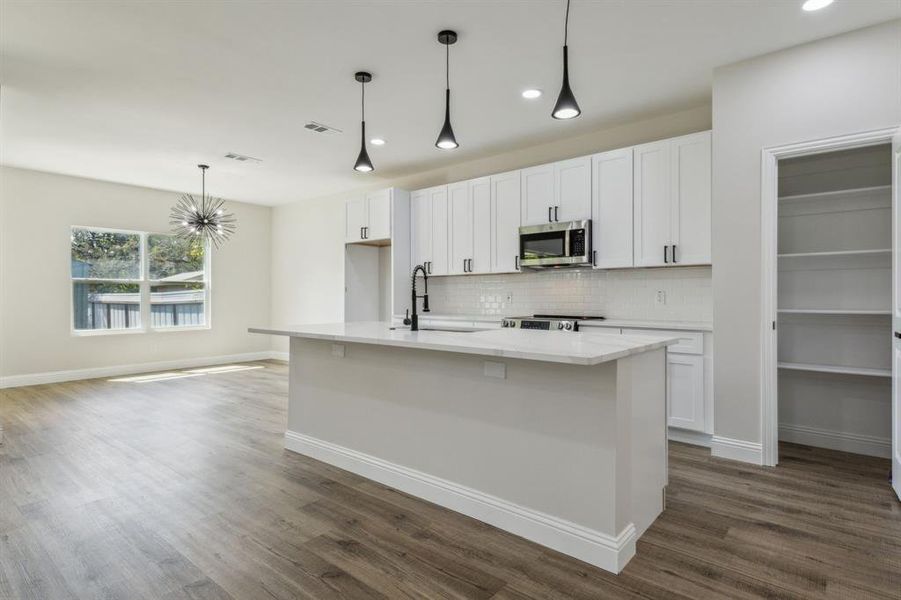 Kitchen with an island with sink, dark hardwood / wood-style flooring, stainless steel appliances, and white cabinets