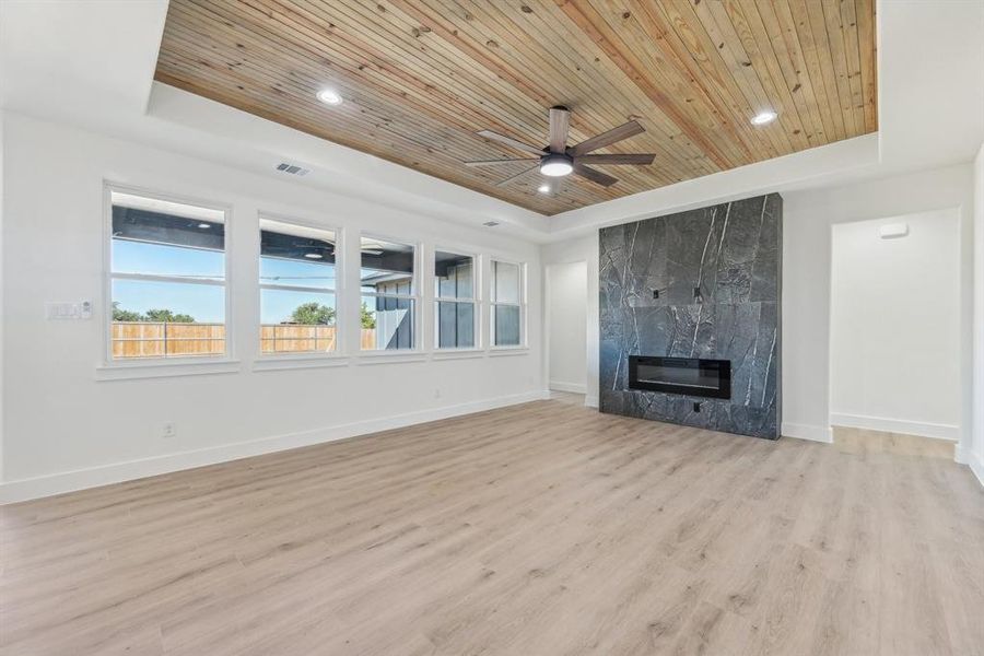 Unfurnished living room with a raised ceiling, a fireplace, wood ceiling, and light wood-type flooring