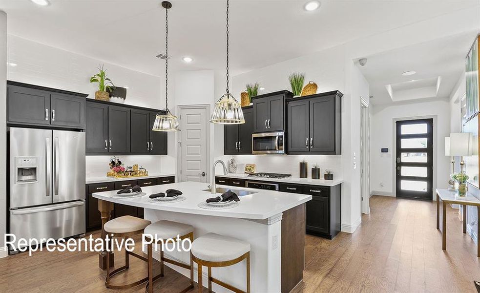 Kitchen with tasteful backsplash, a kitchen island with sink, hardwood / wood-style floors, appliances with stainless steel finishes, and decorative light fixtures