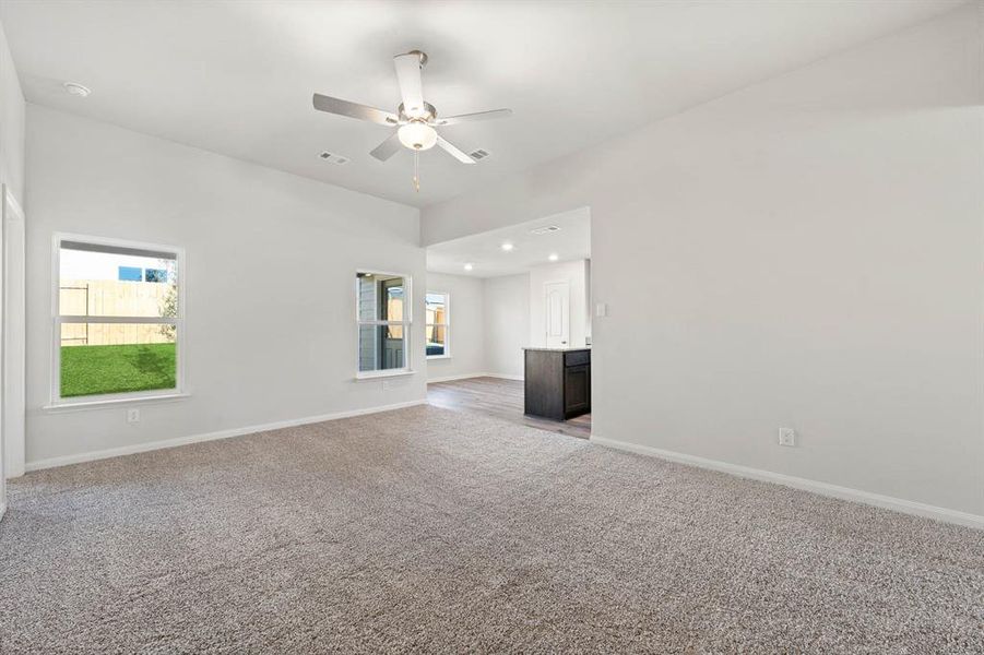 Unfurnished living room featuring ceiling fan, light colored carpet, and a wealth of natural light