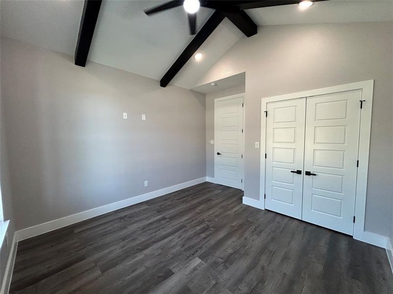 Unfurnished bedroom featuring ceiling fan, a closet, beam ceiling, and dark hardwood / wood-style flooring