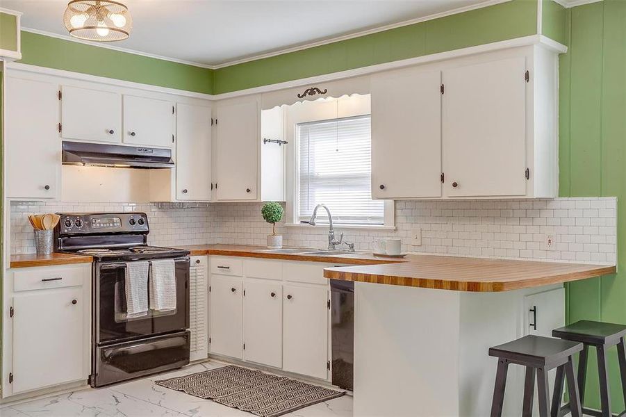 Kitchen with black electric range, backsplash, sink, and white cabinets