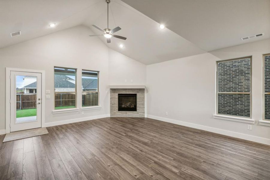 Unfurnished living room featuring a tiled fireplace, ceiling fan, high vaulted ceiling, and dark hardwood / wood-style floors