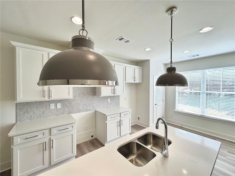 Kitchen featuring hanging light fixtures, sink, light hardwood / wood-style floors, white cabinets, and backsplash