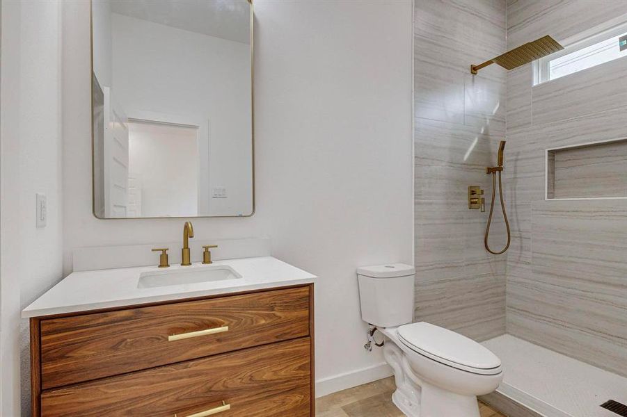 Bathroom featuring a tile shower, vanity, and toilet