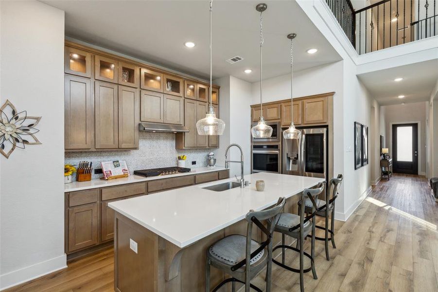 Kitchen featuring a center island with sink, stainless steel appliances, light wood-type flooring, double ovens and decorative backsplash