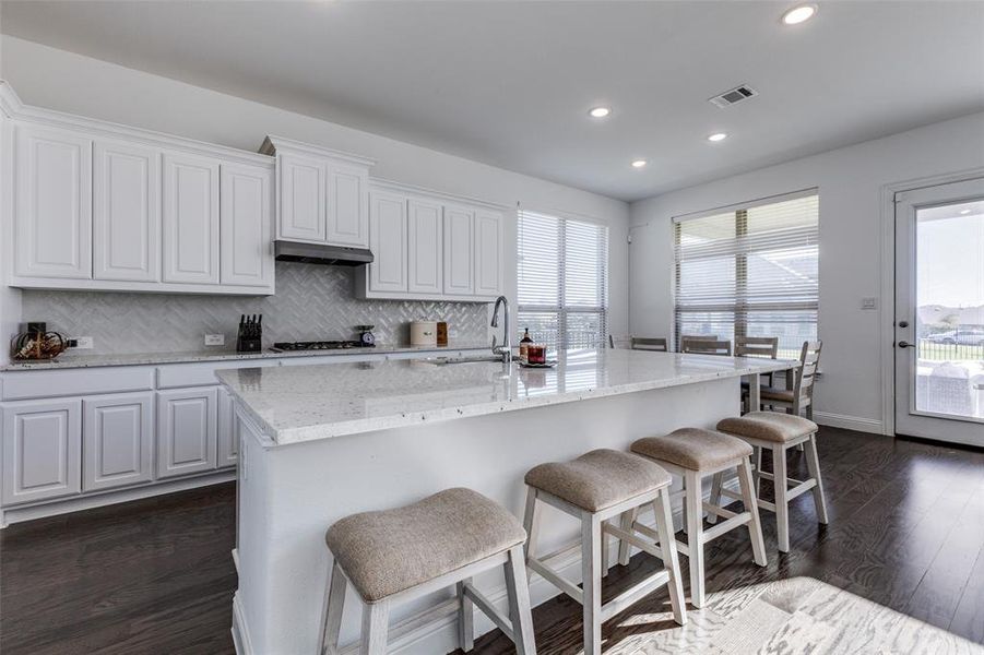 Kitchen featuring a healthy amount of sunlight, white cabinetry, wood flooring and an island with sink