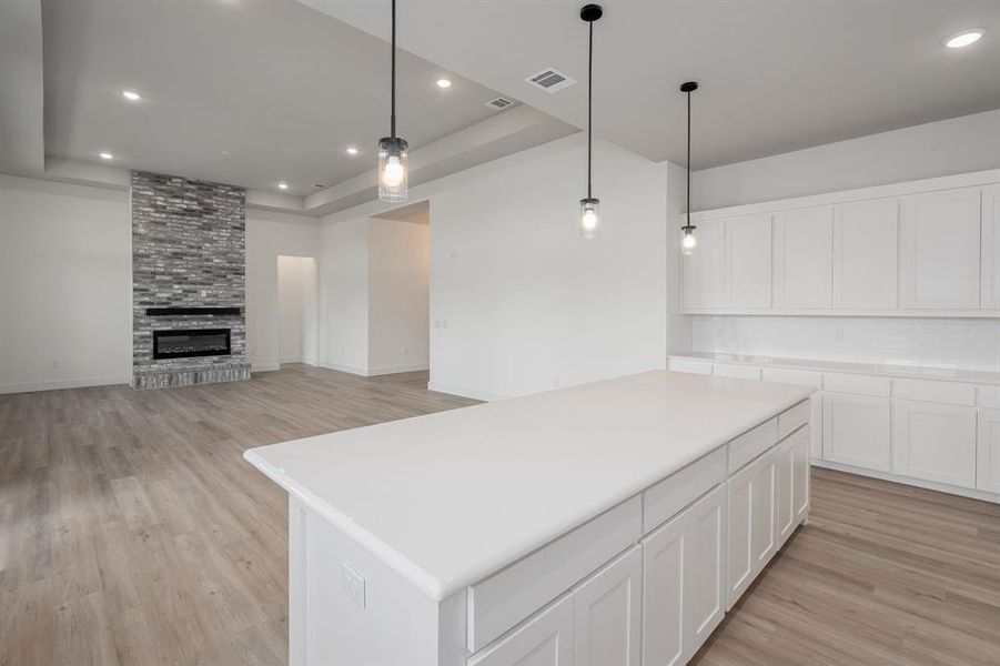 Kitchen featuring white cabinets, hanging light fixtures, a kitchen island, and a fireplace