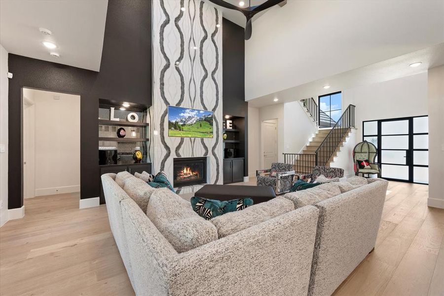 Living room with light wood-type flooring, a towering ceiling, and a large fireplace