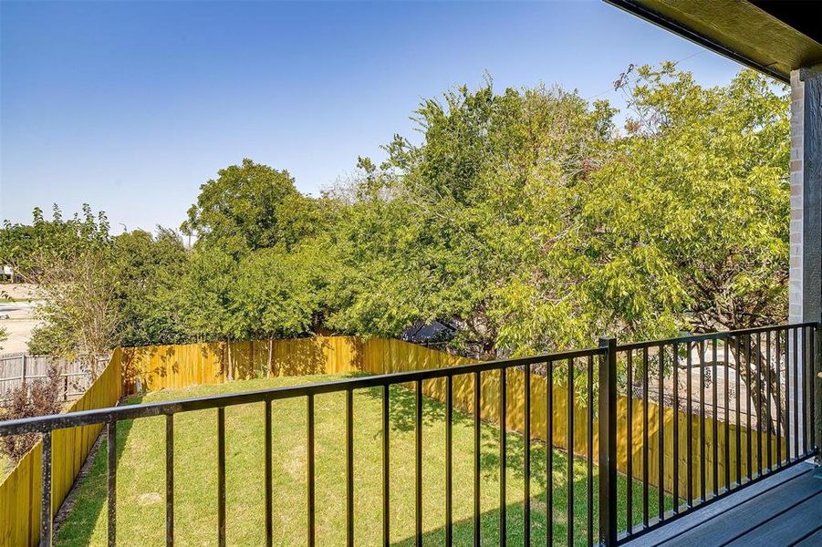 The balcony overlooks the large backyard that is surrounded by mature trees.