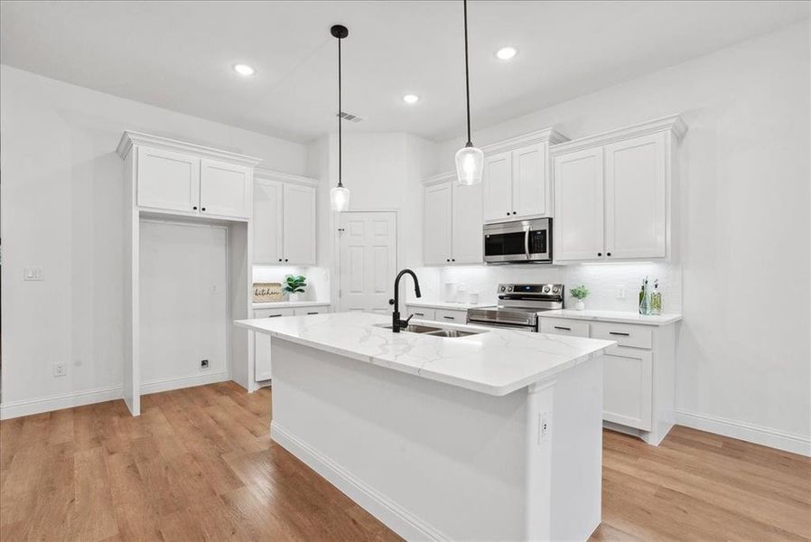 Kitchen featuring light quartz countertops, appliances with stainless steel finishes, an island with sink, sink, and white cabinetry