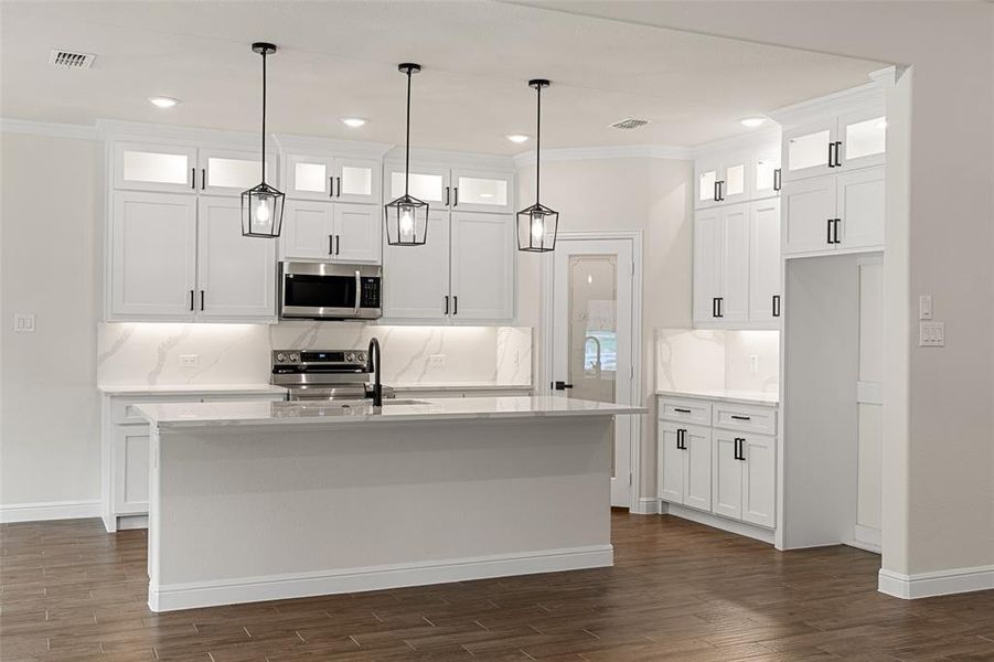 Kitchen featuring appliances with stainless steel finishes, white cabinets, decorative backsplash, and a kitchen island with sink