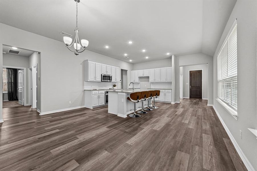 Kitchen with dark hardwood / wood-style flooring, a chandelier, white cabinetry, a kitchen bar, and a center island with sink