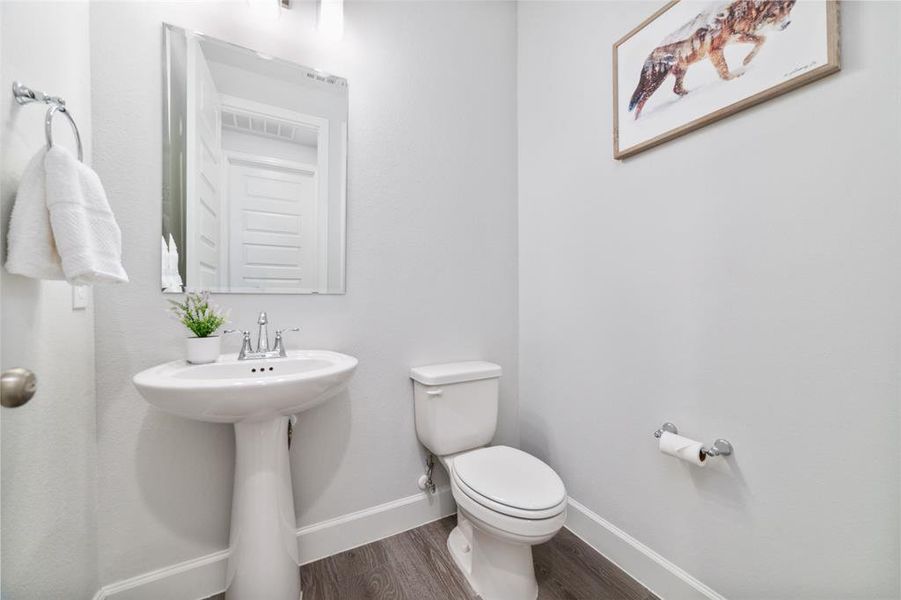 Modern half-bathroom featuring a pedestal sink, toilet, and a framed wall mirror.
