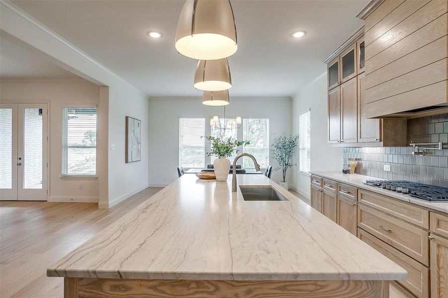 Kitchen featuring light hardwood flooring, a kitchen island with leathered Quartzite countertops, farm sink, natural stain custom cabinetry with soft close drawers and cabinets.