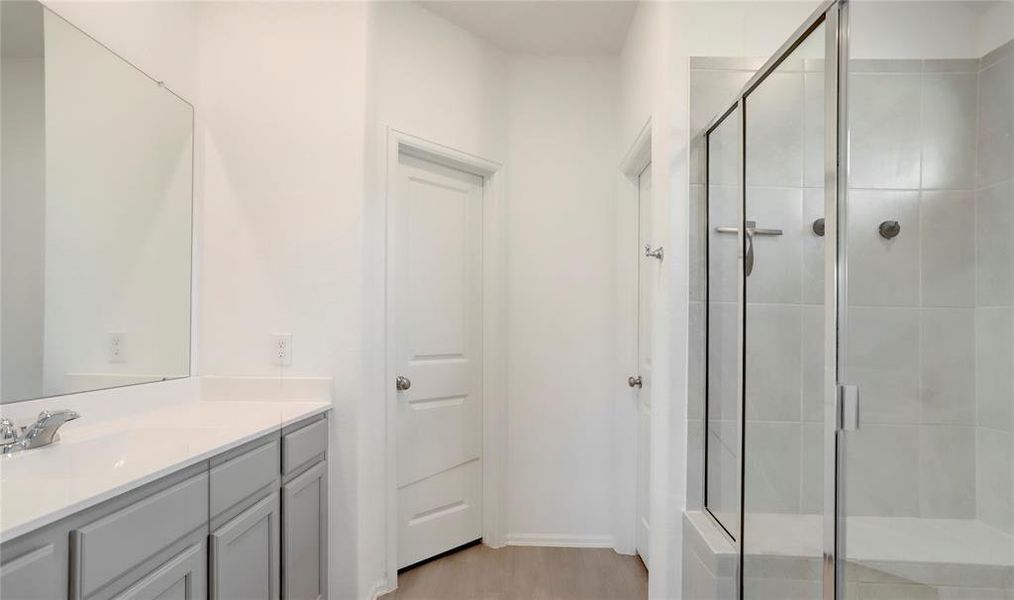 THE PRIMARY BATHROOM FEATURES A SLEEK WALK-IN SHOWER WITH GLASS DOORS AND A LONG VANITY WITH AMPLE COUNTER SPACE.