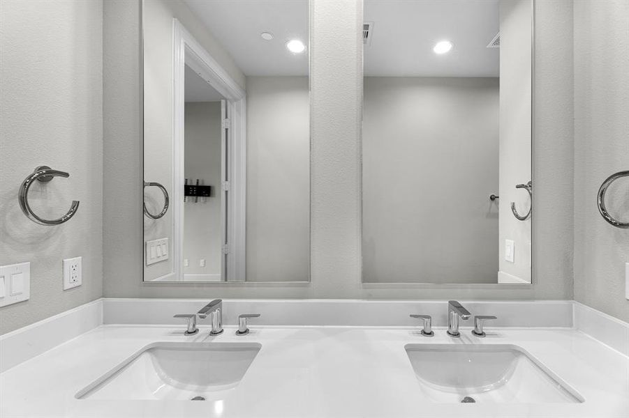 Dual sinks are elegantly positioned below a large mirror, offering both convenience and style. The luxurious quartz countertops elevate the space, providing a polished finish that enhances the bathroom's modern aesthetic.