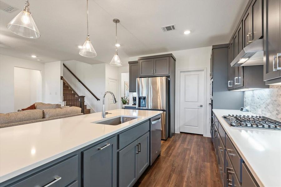 Kitchen featuring dark hardwood / wood-style flooring, sink, decorative light fixtures, stainless steel appliances, and ventilation hood