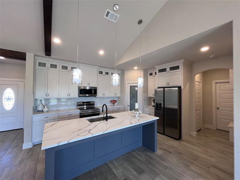 Kitchen with appliances with stainless steel finishes, a kitchen island with sink, and white cabinetry