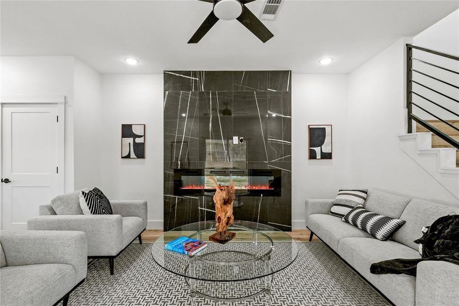 Living room with ceiling fan, a tiled fireplace, and hardwood / wood-style floors