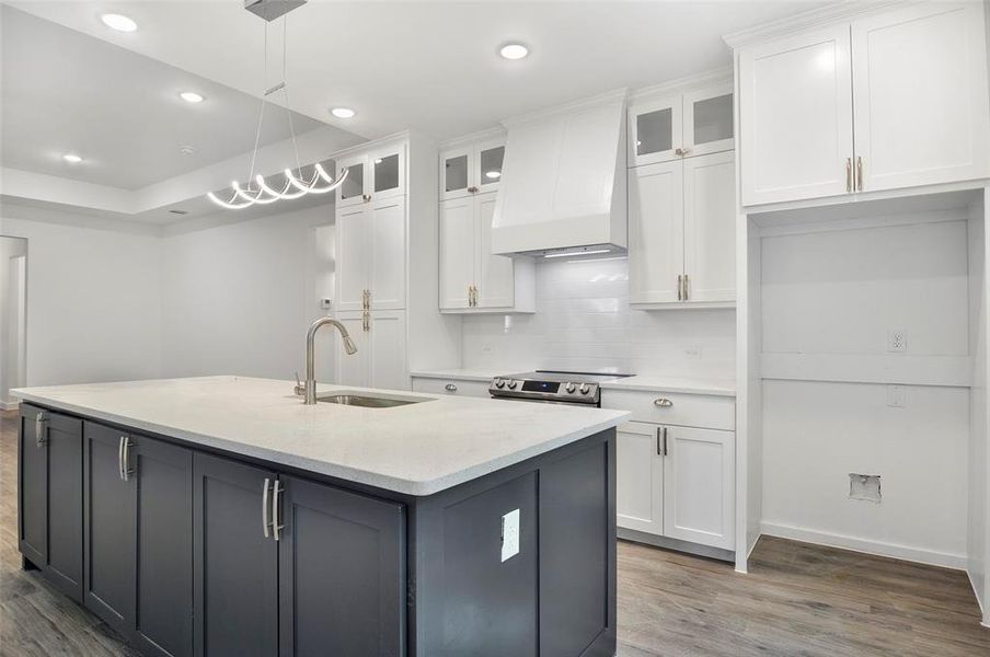 Kitchen featuring white cabinetry, custom range hood, pendant lighting, wood-type flooring, and sink