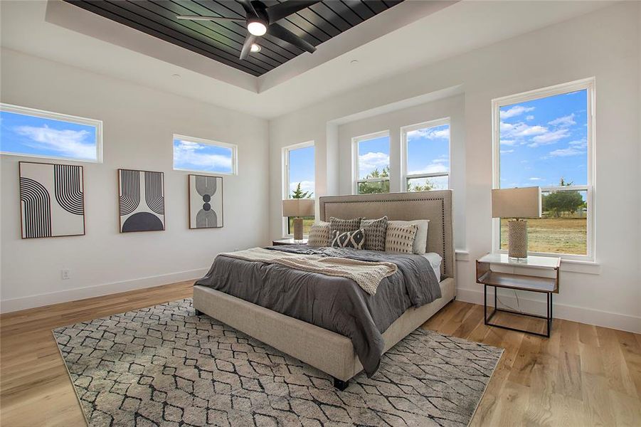 Bedroom featuring ceiling fan, a tray ceiling, and light wood-type flooring